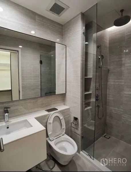 Condominium for rent in Bang Rak, Bangkok - Modern bathroom with large mirror, vanity and a glass-enclosed rain shower.