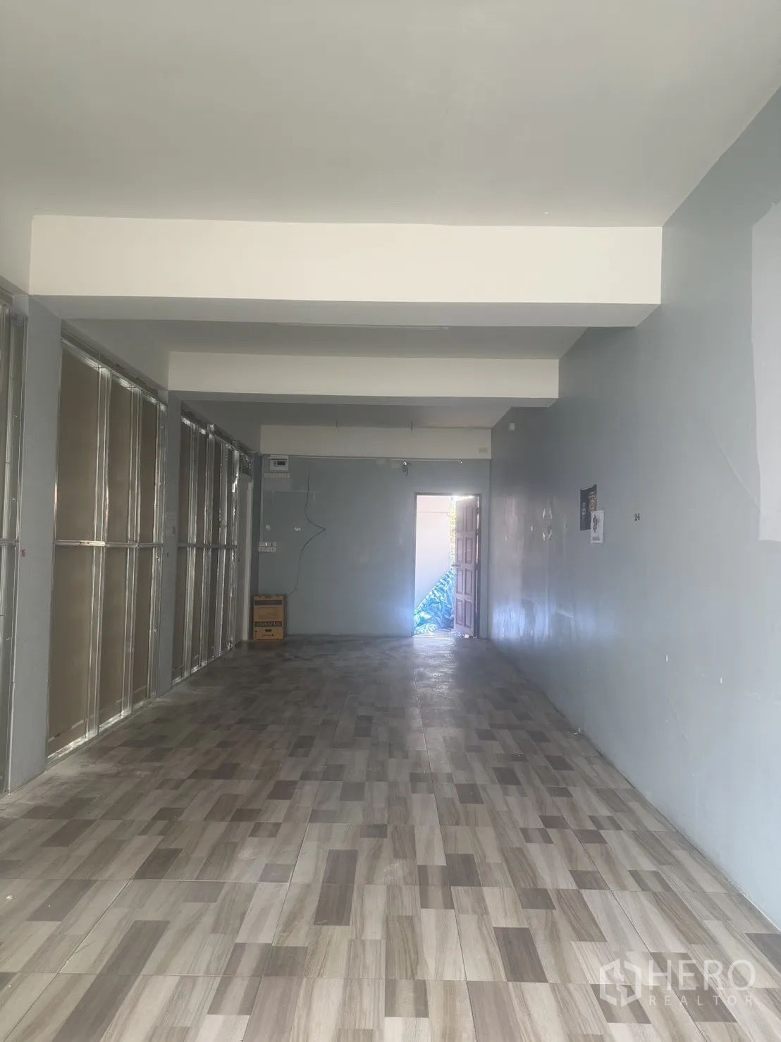 零售空间 for rent in Pathum Wan, Bangkok - 开放式零售室内空间，木纹地砖与浅灰墙面，尽端有后部门口采光。