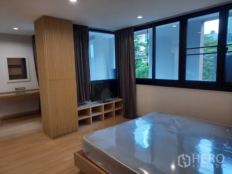 Condominium for rent in Watthana, Bangkok - Spacious bedroom with large windows, curtains, built-in TV stand and a queen bed on wooden flooring.