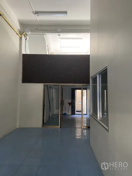 Shophouse for rent in Bang Na, Bangkok - Ground-floor hall with high ceiling, blue tiles and sliding glass partitions leading to the rear area.