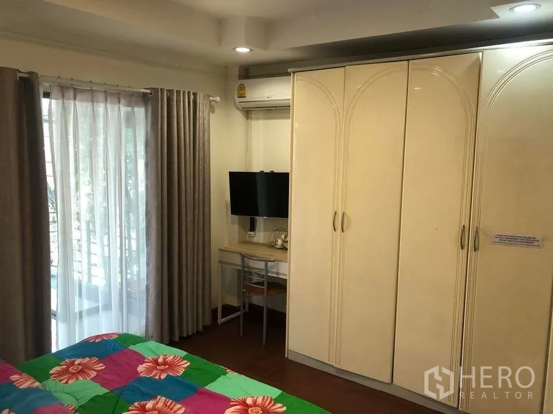 Retail Space for rent in Khlong Toei, Bangkok - Bedroom with wardrobe, TV and work desk opening to a balcony with sheer curtains.