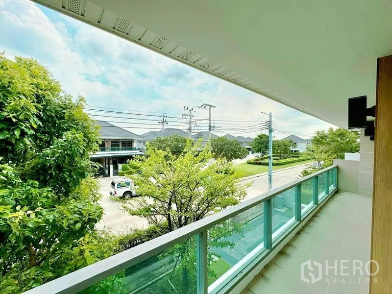 独立式住宅 出售在Lat Krabang, Bangkok - 玻璃栏杆的二楼阳台，眺望绿荫街景。