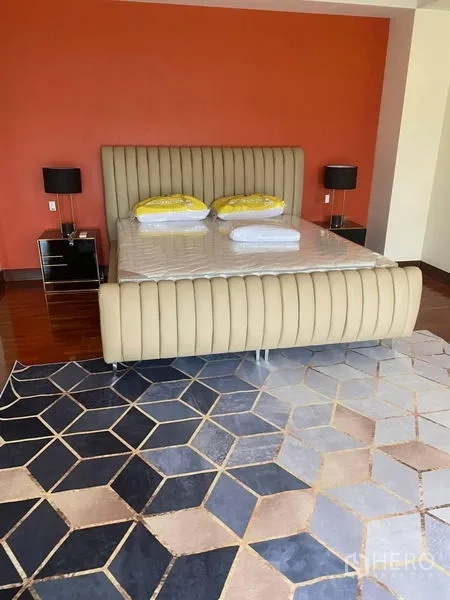 Detached House for rent in Suan Luang, Bangkok - Master bedroom with upholstered bed, orange accent wall and geometric rug on wood floors.