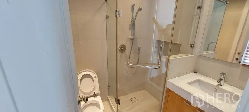 公寓 出租在Pathum Wan, Bangkok - 紧凑浴室，玻璃干湿分离淋浴间，白色盥洗台与镜柜，浅色墙面。