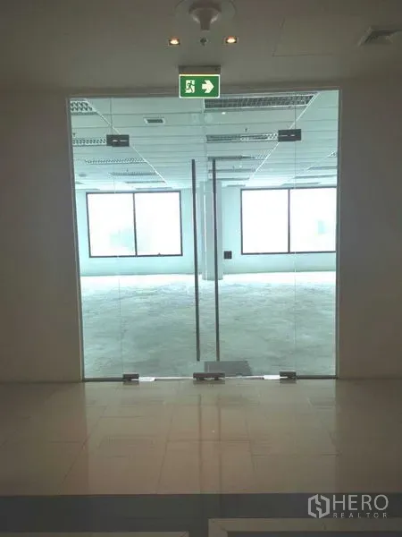办公空间 出租在Chatuchak, Bangkok - 大楼大堂进入办公室的玻璃双开门入口，上方设有紧急出口标识。