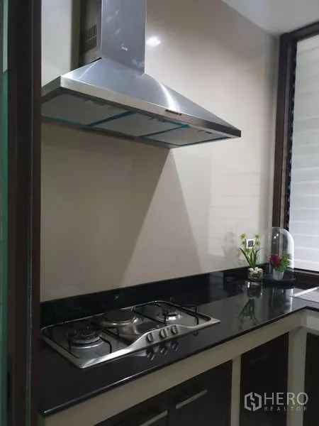 独立式住宅 出售在Watthana, Bangkok - 紧凑厨房，黑色石材台面，燃气灶与不锈钢抽油烟机。
