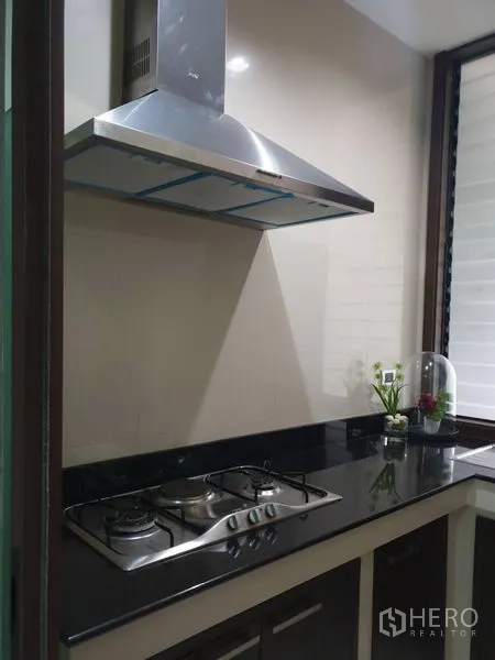 独立式住宅 出售在Watthana, Bangkok - 紧凑厨房，黑色石材台面，燃气灶与不锈钢抽油烟机。