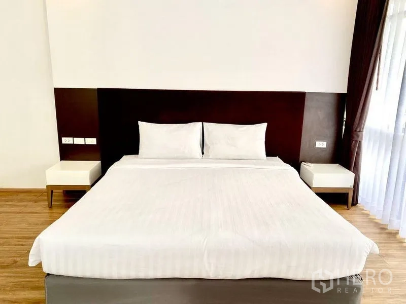 Condominium for rent in Khlong Toei, Bangkok - Bedroom with king bed, dark headboard, bedside tables and balcony window.