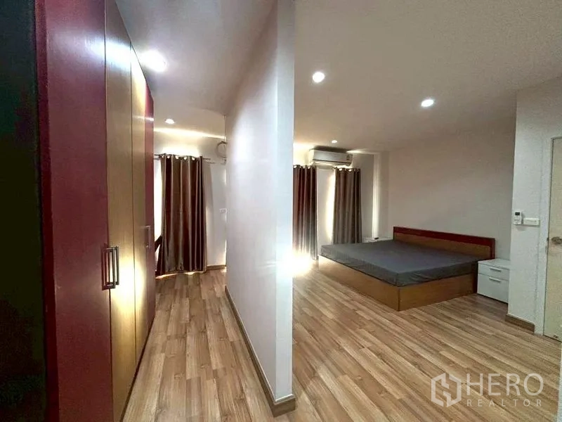 Townhouse for rent in Suan Luang, Bangkok - Large bedroom with wood flooring, curtains, and bed frame.