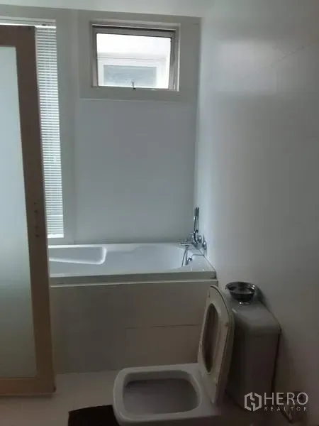 Condominium for rent in Ratchathewi, Bangkok - White bathroom featuring a bathtub beneath a small window and a frosted sliding door.