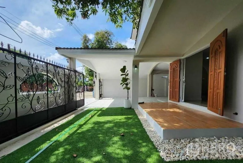 Detached House for rent in Lam Luk Ka, Pathum Thani - Side yard with artificial lawn, terrace and decorative iron gate.