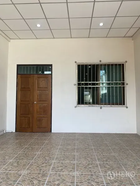 Townhouse for rent in Suan Luang, Bangkok - Covered front porch with patterned tiles, solid wooden door and barred window of the townhouse.