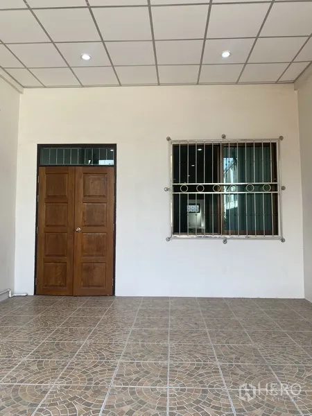 Townhouse for rent in Suan Luang, Bangkok - Covered front porch with patterned tiles, solid wooden door and barred window of the townhouse.