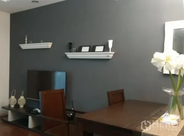 公寓 出租在Khlong Toei, Bangkok - 餐桌与电视柜相邻，灰色主墙搭配悬浮层板装饰。