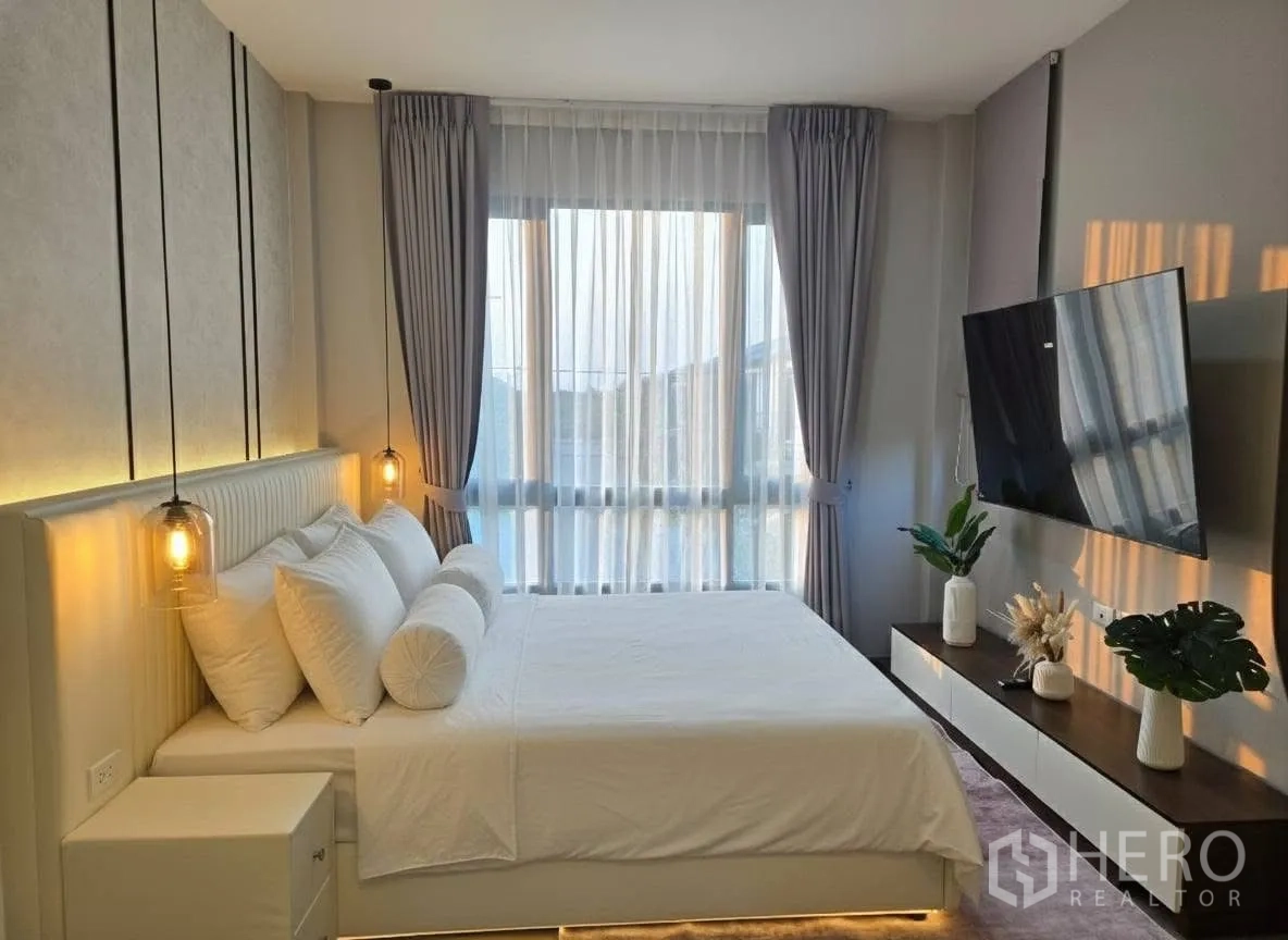 บ้าน for rent or sale in Bang Phli, Samut Prakan - ห้องนอนใหญ่มีโคมไฟห้อยข้างเตียง ทีวีติดผนัง และหน้าต่างเต็มบาน