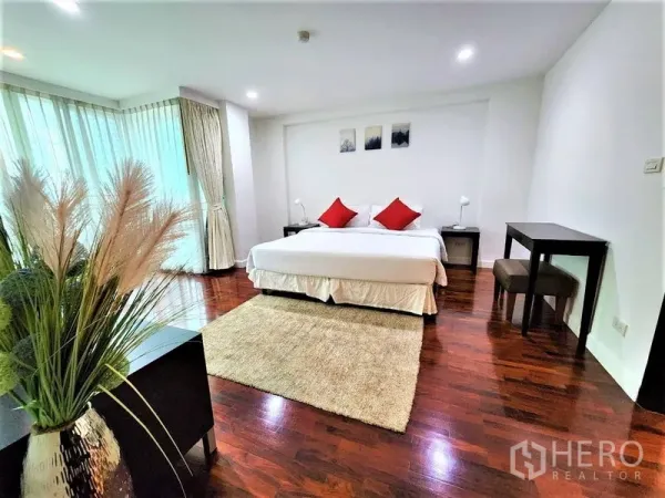 Condominium for rent in Bang Rak, Bangkok - Spacious master bedroom with a king bed, red cushions, corner windows with curtains and glossy wooden flooring.