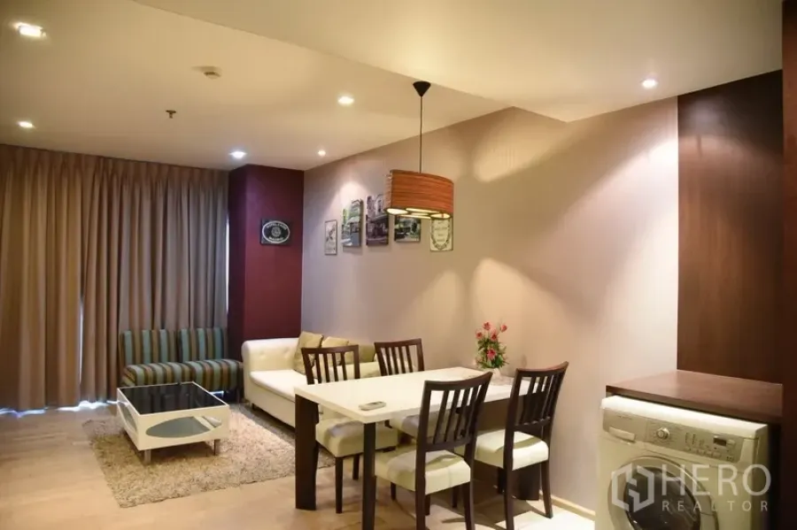 Condominium for rent in Khlong Toei, Bangkok - Open-plan living and dining area with sofa, four-seat table, and floor-to-ceiling curtains in a modern Bangkok condo.