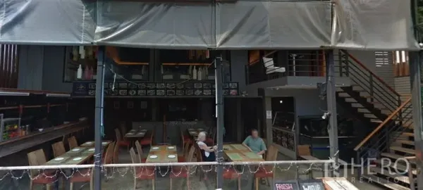 零售空间 出租在Khlong Toei, Bangkok - 挑高室内，餐饮式布局，木质餐桌与通往夹层的楼梯。