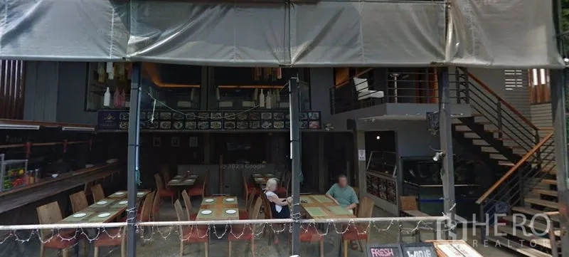 零售空间 出租在Khlong Toei, Bangkok - 挑高室内，餐饮式布局，木质餐桌与通往夹层的楼梯。
