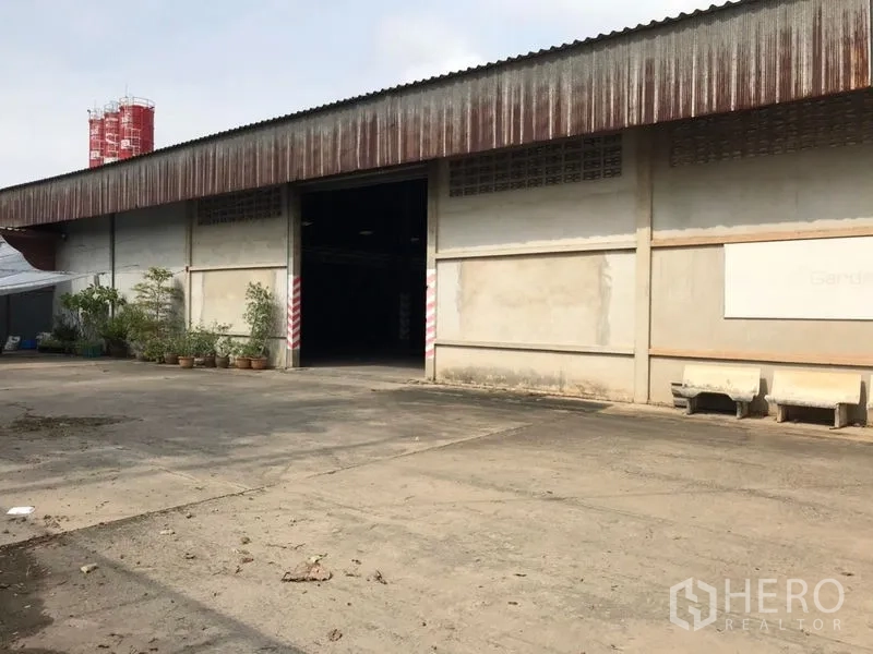 Warehouse for rent in Mueang Nakhon Pathom, Nakhon Pathom - Warehouse frontage with open bay, concrete yard and greenery.