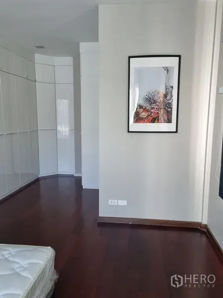 Detached House for sale in Chatuchak, Bangkok - Bedroom with dark wood flooring, white built-in wardrobes and framed wall art.