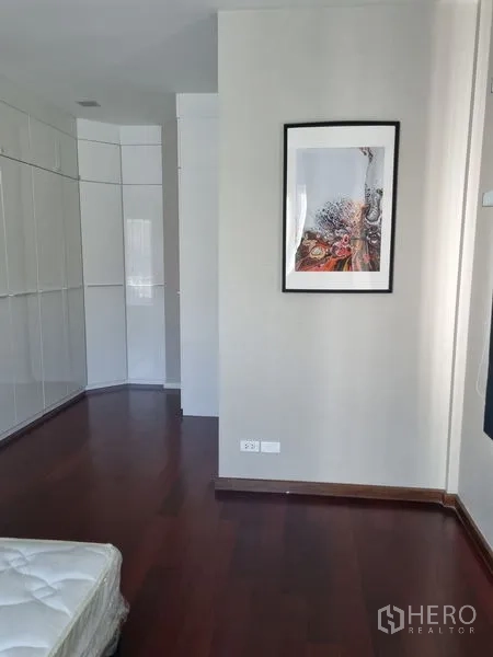 Detached House for sale in Chatuchak, Bangkok - Bedroom with dark wood flooring, white built-in wardrobes and framed wall art.