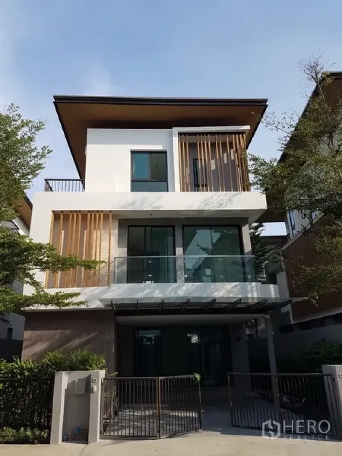 บ้าน ให้เช่าในPrawet, Bangkok - บ้านเดี่ยวสไตล์โมเดิร์นสูงสามชั้น พร้อมระเบียงกระจก ซี่ไม้ตกแต่ง และที่จอดรถหน้าบ้านมีรั้วกั้น.
