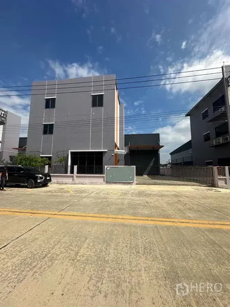 工厂 出租在Lam Luk Ka, Pathum Thani - 蓝天之下的三层办公楼与工厂外立面，带有大门和车道