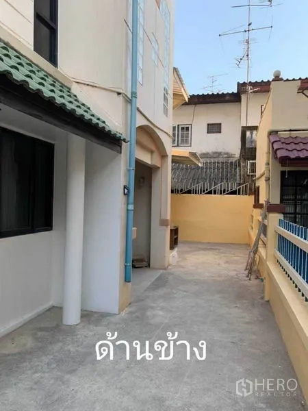 Townhouse for rent in Phra Khanong, Bangkok - Side exterior alley of the townhouse with cream walls, tiled eaves, and a gated walkway.
