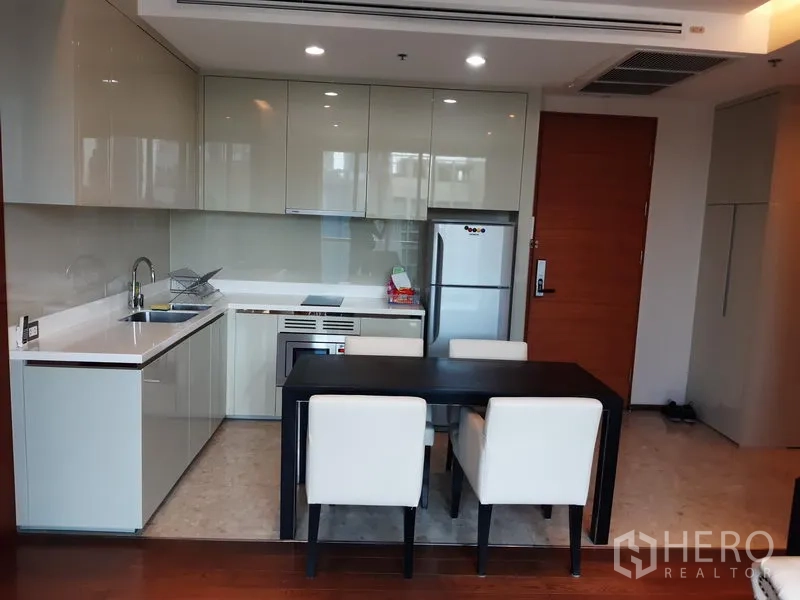Condominium for rent in Khlong Toei, Bangkok - Modern open kitchen with glossy cabinets, cooktop, stainless fridge and a four-seat dining table.