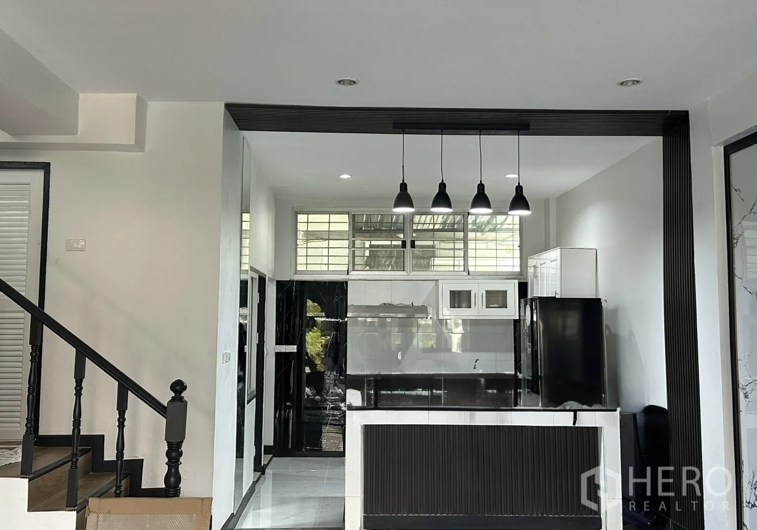 联排别墅 for rent in Watthana, Bangkok - 黑白配色厨房，岛台、吊灯与高窗。