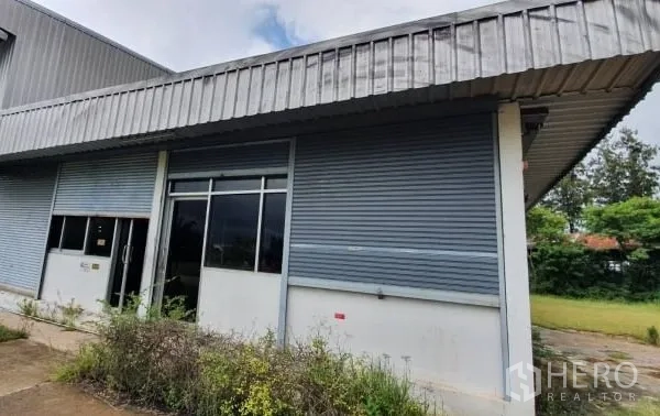 货栈 出租在Chaloem Phra Kiat, Nakhon Ratchasima - 仓库正面设办公区窗户与金属卷帘门入口。