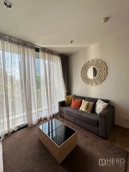 Condominium for rent in Watthana, Bangkok - Living and dining area with large windows, brown rug, and compact dining set.