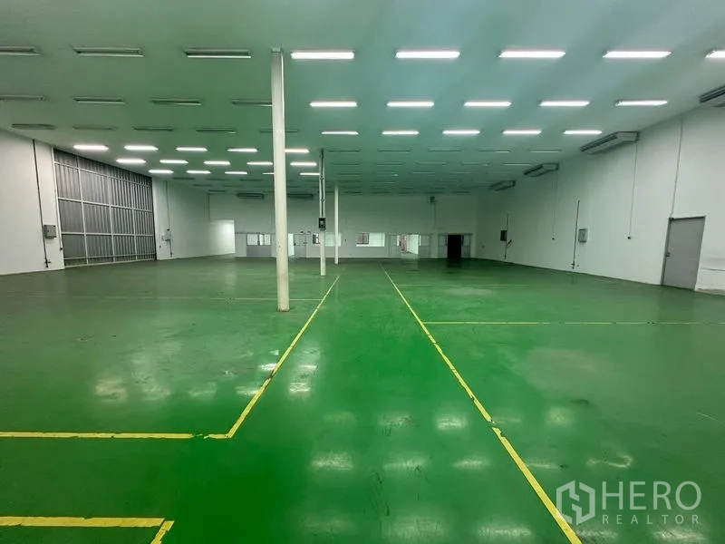 Warehouse for rent in Suan Luang, Bangkok - Wide warehouse bay with green floor and a roller shutter door.
