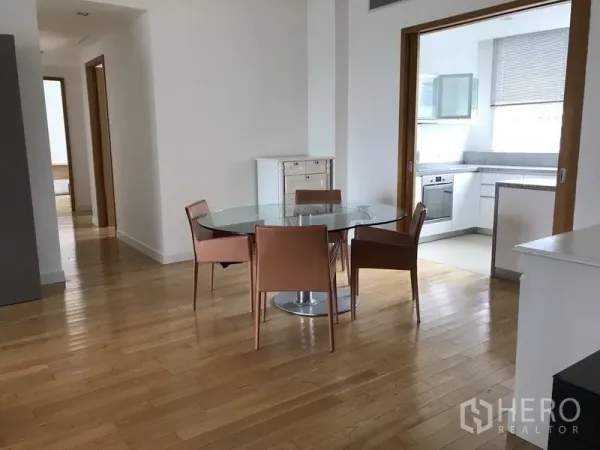 Condominium for rent in Khlong Toei, Bangkok - Dining zone with round glass table and four chairs beside sliding doors to the closed kitchen.