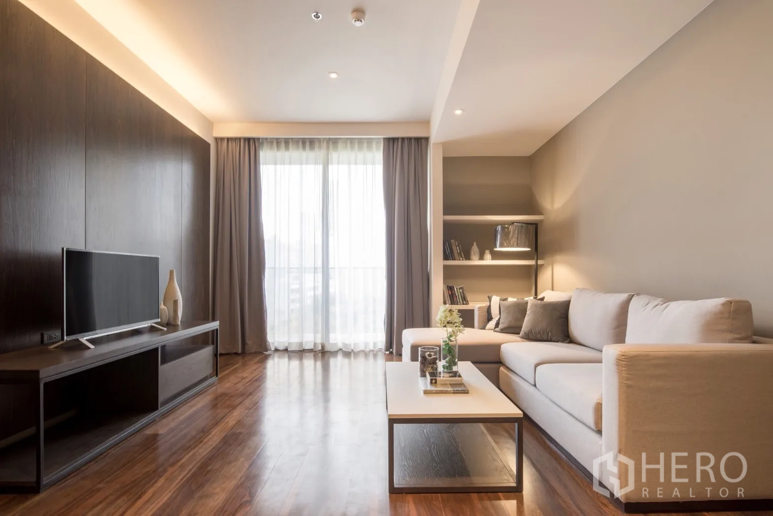 Condominium for rent in Khlong Toei, Bangkok - Contemporary lounge with built-in shelving, TV console and sheer curtains allowing natural light.
