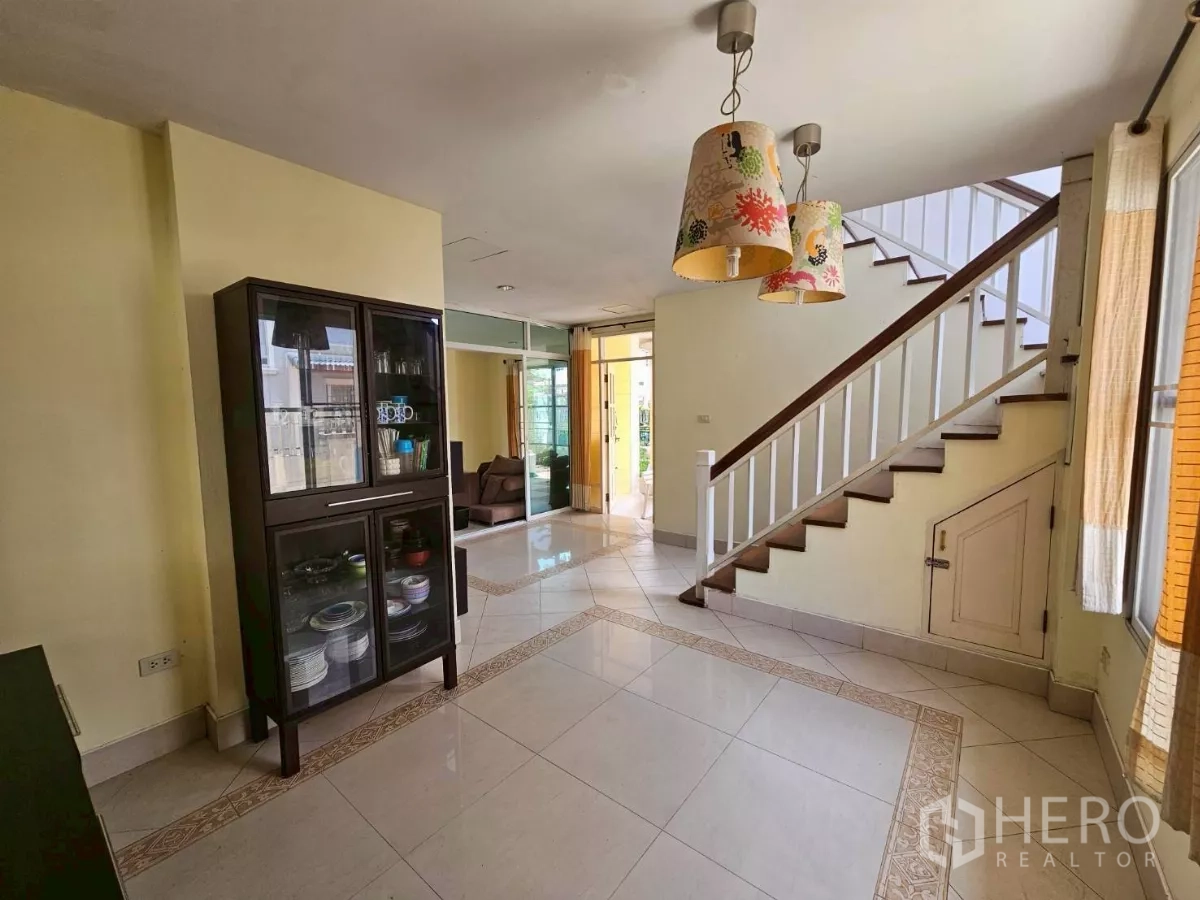 Detached House for rent or sale in Bang Lamung, Chon Buri - Dining area near the stairs featuring pendant lights and a glass cabinet.