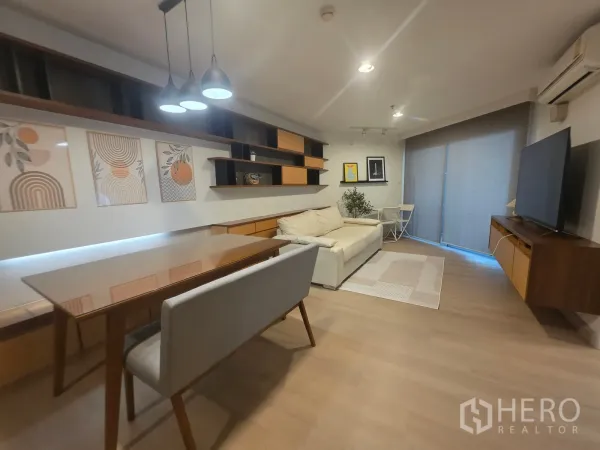 Condominium for rent in Huai Khwang, Bangkok - Living and dining area with sofa, TV console, and sliding door to the balcony.