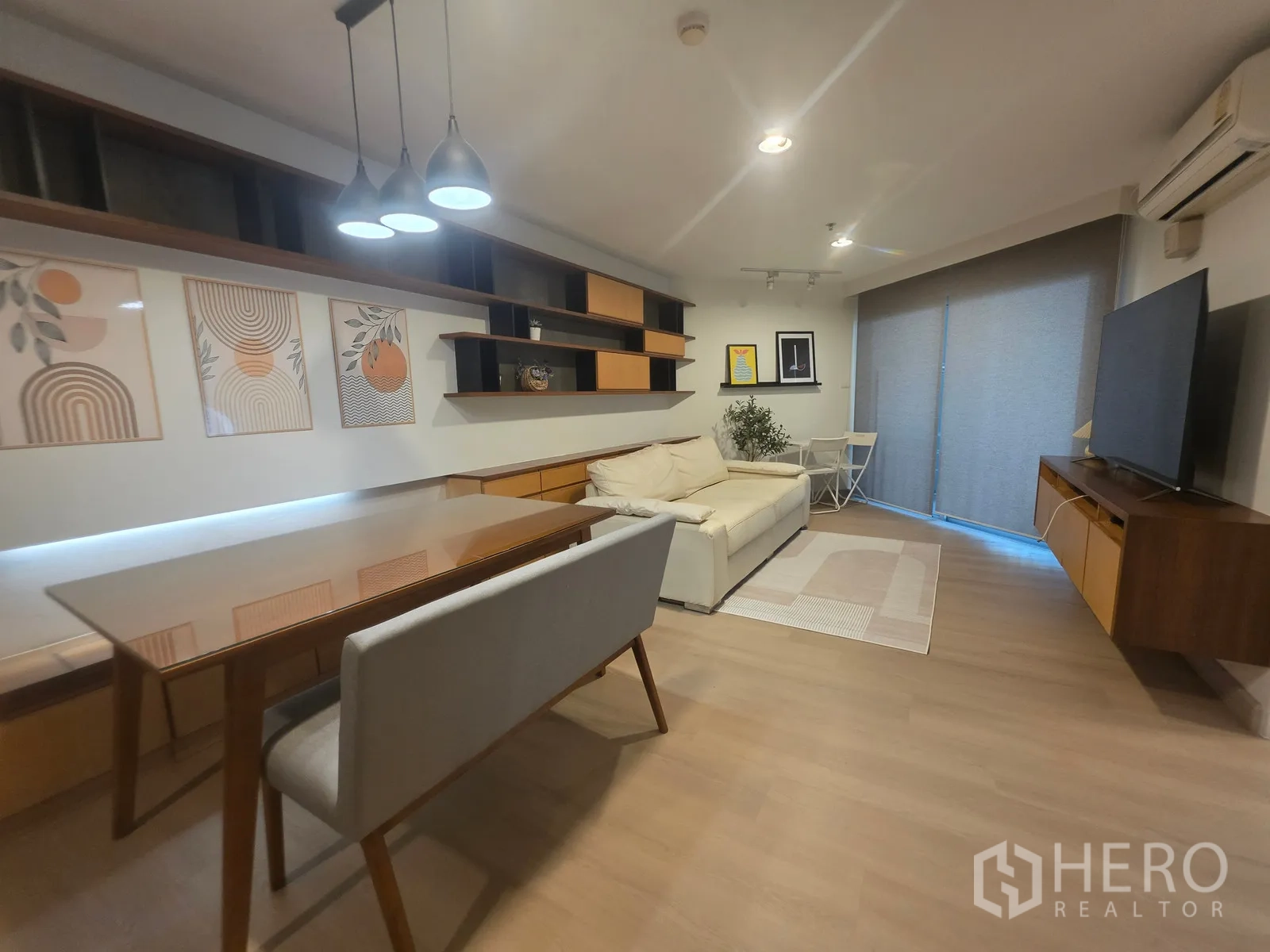 Condominium for rent in Huai Khwang, Bangkok - Living and dining area with sofa, TV console, and sliding door to the balcony.