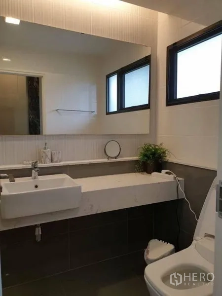 Detached House for rent in Bang Phli, Samut Prakan - Contemporary bathroom with large mirror, window, sink and toilet.