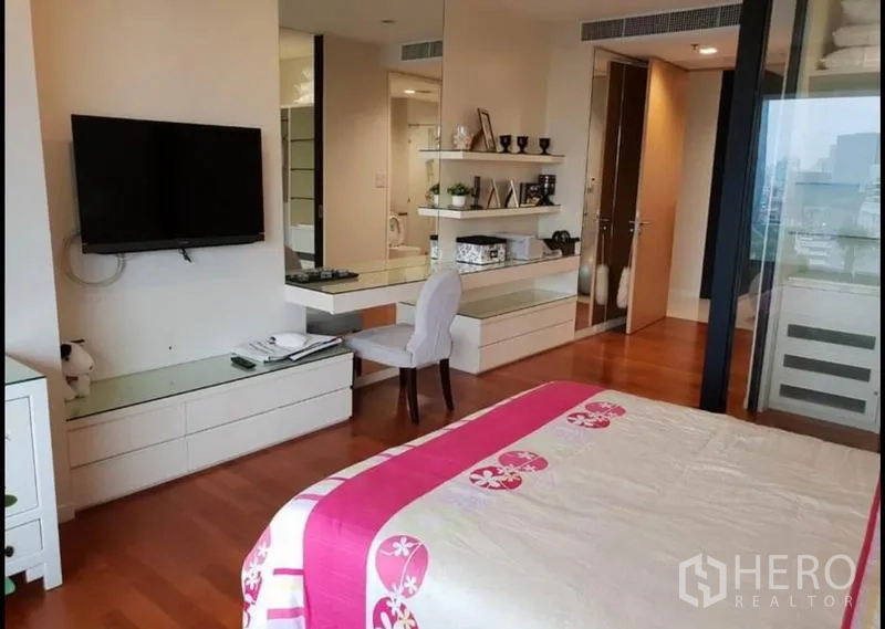 Condominium for rent in Sathon, Bangkok - Bedroom angle showing wall-mounted TV, vanity desk, shelves and city outlook.