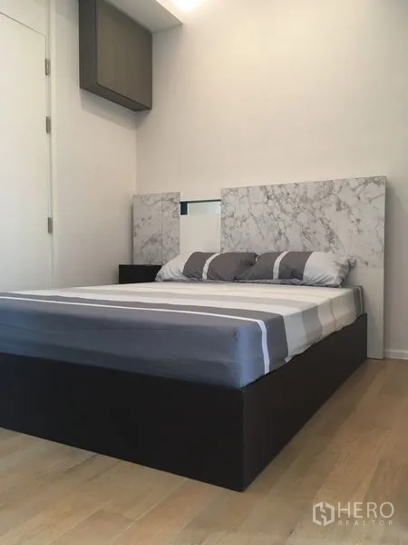 Condominium for rent or sale in Chatuchak, Bangkok - Minimalist bedroom with a marble-look headboard, striped bedding and light wood floors.