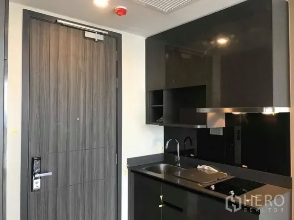 Condominium for rent in Watthana, Bangkok - Entry door beside built-in kitchenette with black cabinetry and range hood.