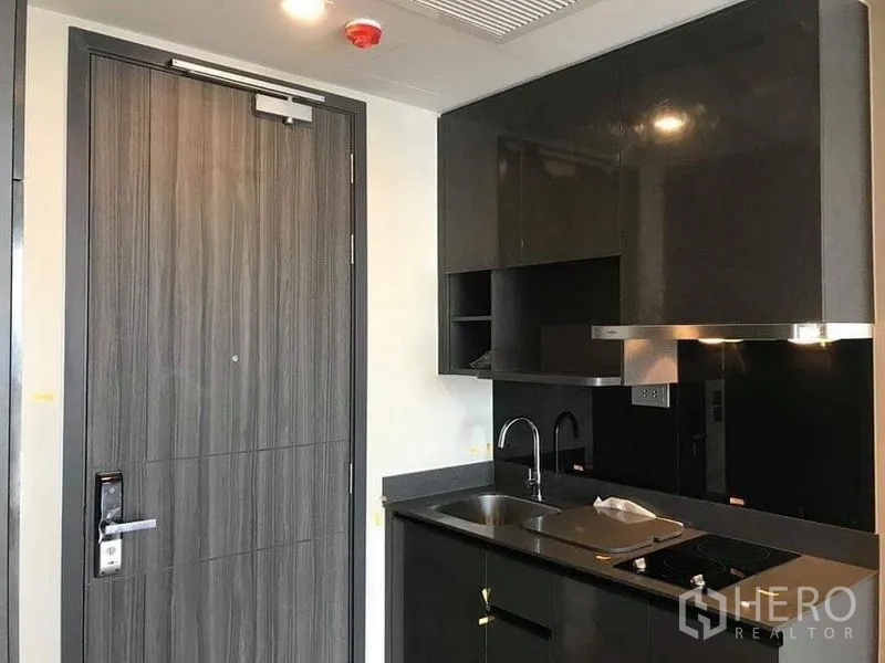 Condominium for rent in Watthana, Bangkok - Entry door beside built-in kitchenette with black cabinetry and range hood.
