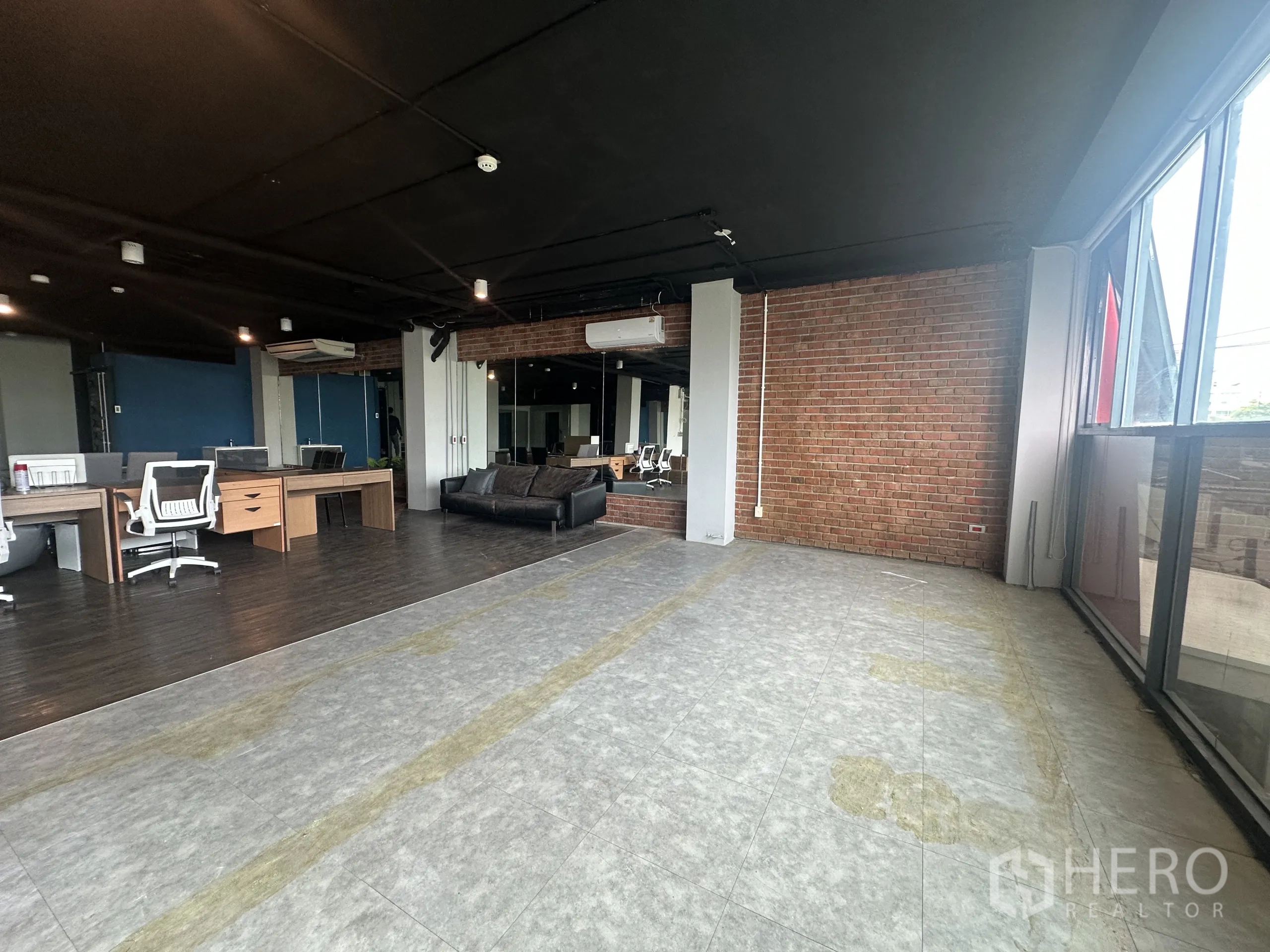 办公空间 出租在Watthana, Bangkok - 转角工作区，大窗、砖墙与瓷砖地面，毗邻办公工位。