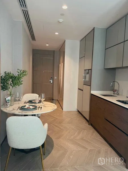 Condominium for rent in Khlong Toei, Bangkok - Compact dining nook for two beside a galley kitchen with herringbone wood floors.