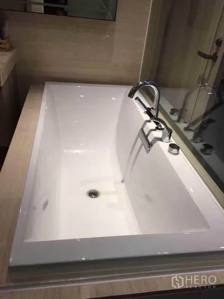 Condominium for rent in Watthana, Bangkok - White rectangular bathtub with chrome faucet in a tiled bathroom.