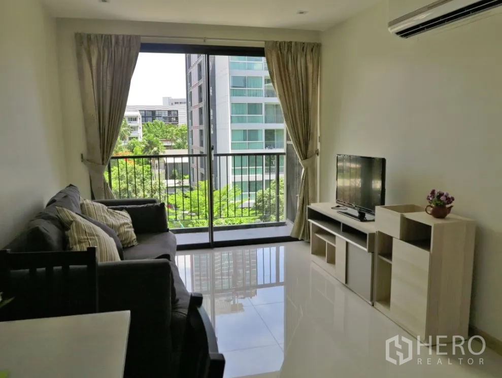 Condominium for rent or sale in Watthana, Bangkok - Bright living room with sofa, TV console, and sliding doors to a balcony overlooking greenery in a Watthana condo near BTS Ekkamai.
