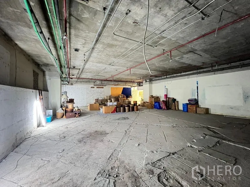 Retail Space for rent - Spacious unfinished retail unit with exposed concrete ceiling, visible pipes and an open-plan floor with boxes.
