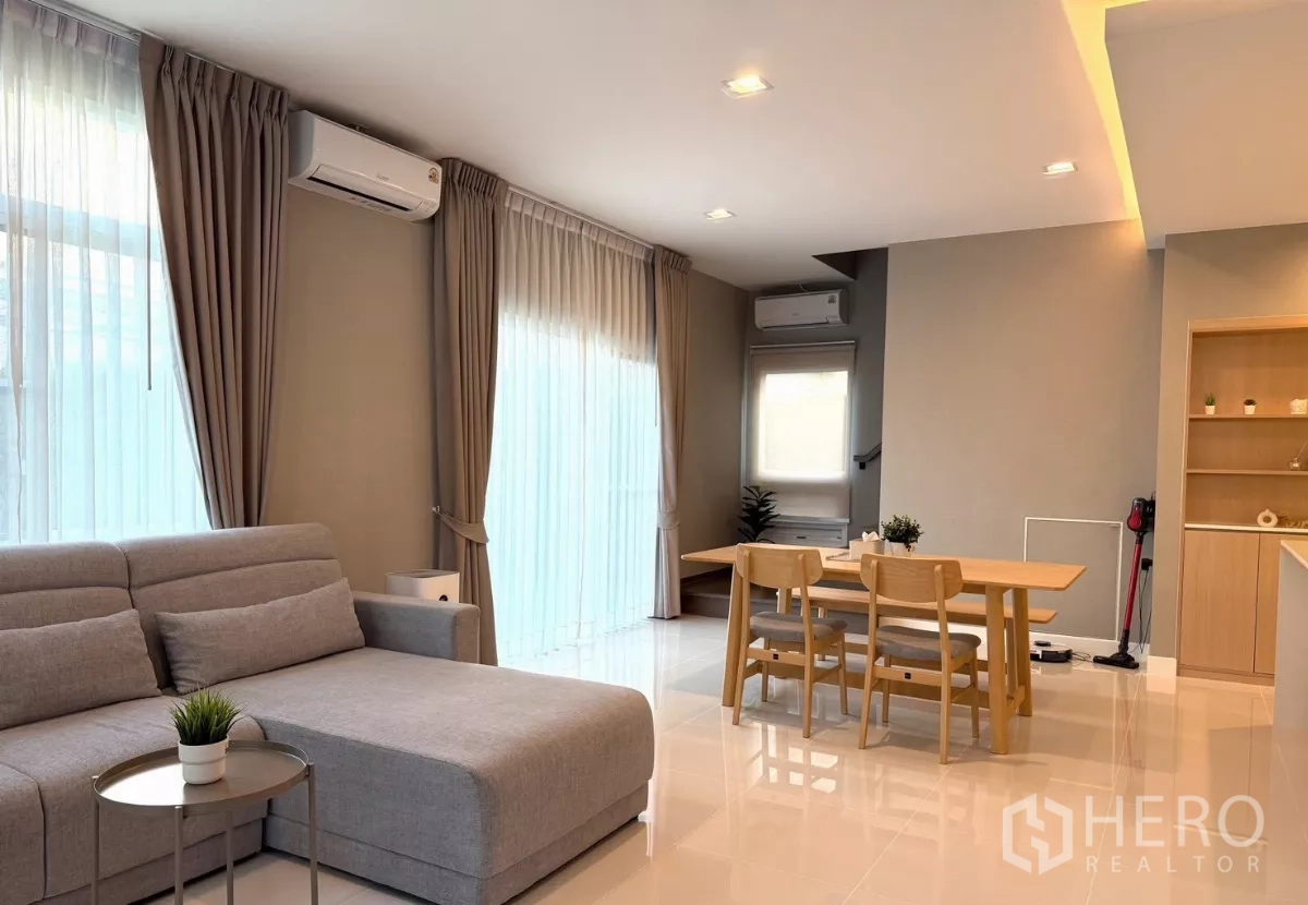 独立式住宅 出租在Prawet, Bangkok - 明亮客厅配灰色转角沙发、餐桌与落地窗帘